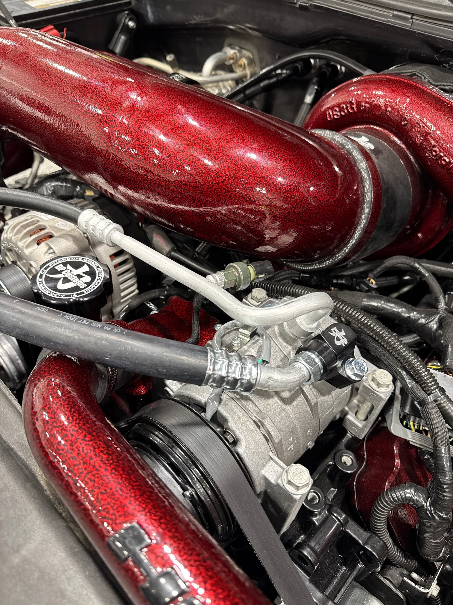 DP Customs Duramax 03-07 front route AC suction line installed in engine bay, showcasing durable aluminum construction and fittings