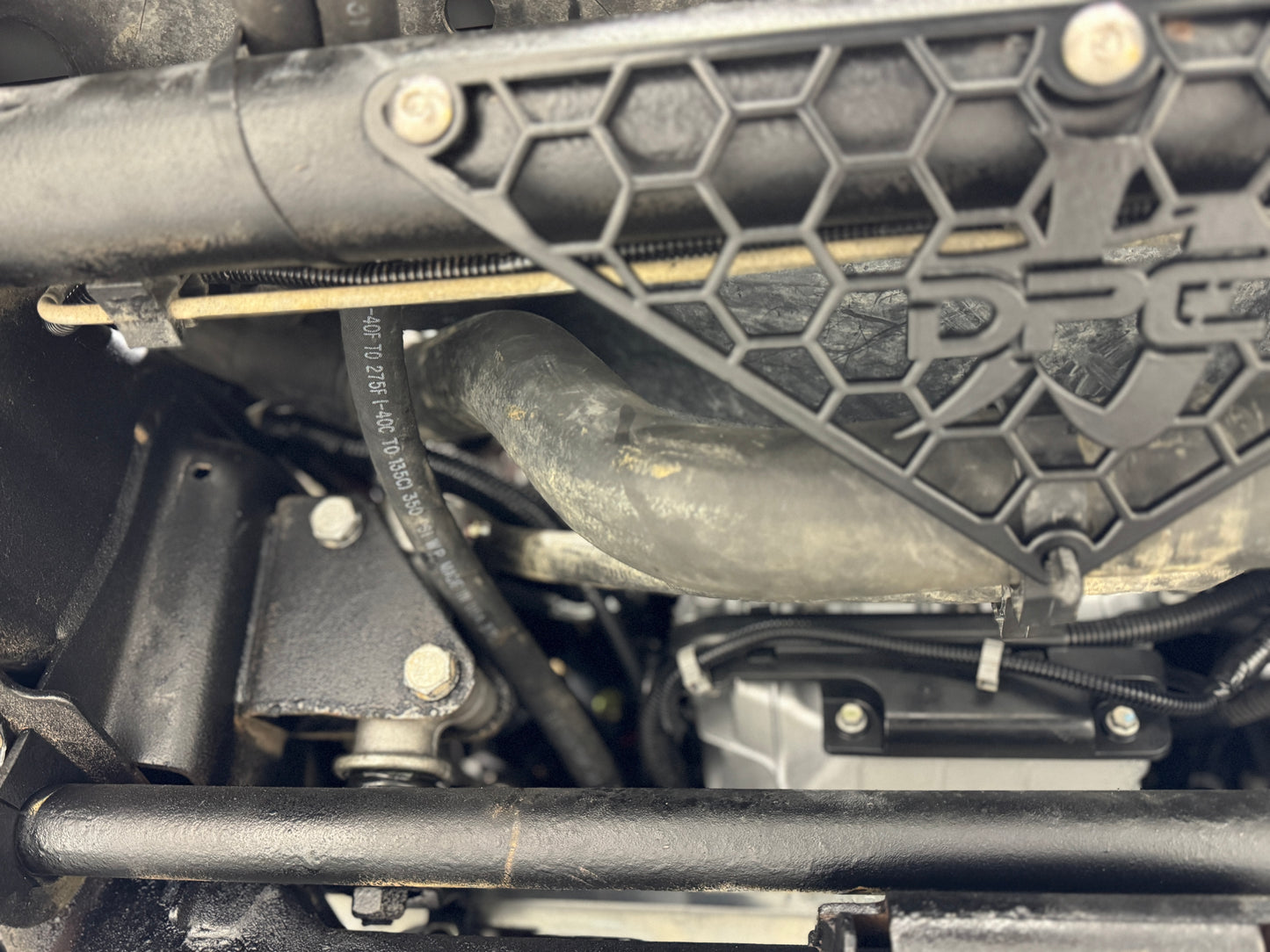 DP Customs radiator hose support bracket for 2001-2010 Duramax engines, mounted on engine bay with hoses attached.