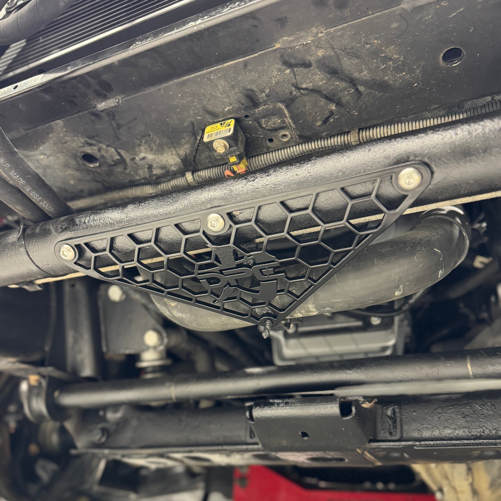DP Customs Duramax radiator hose support bracket for 2001-2010 models, shown installed on engine for secure hose positioning.