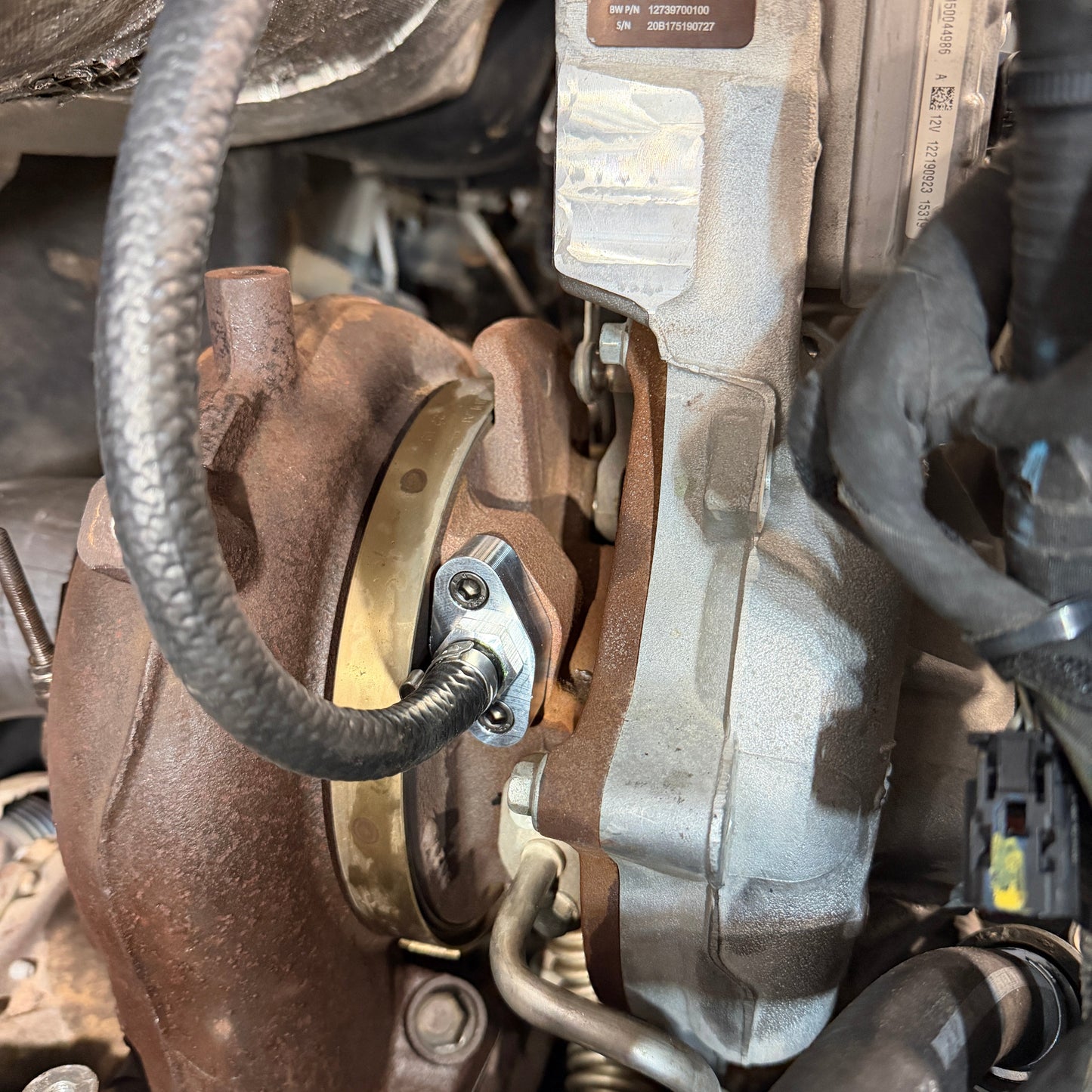 DP Customs L5P Duramax VGT coolant return adapter fitting shown, metal component with threaded connections for diesel engine cooling system