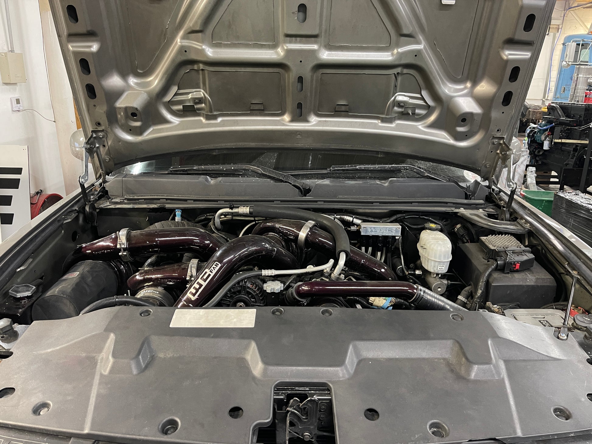 DP Customs high access hood brackets installed on a 2007.5-2016 GM truck, showing sturdy metal brackets under the hood.