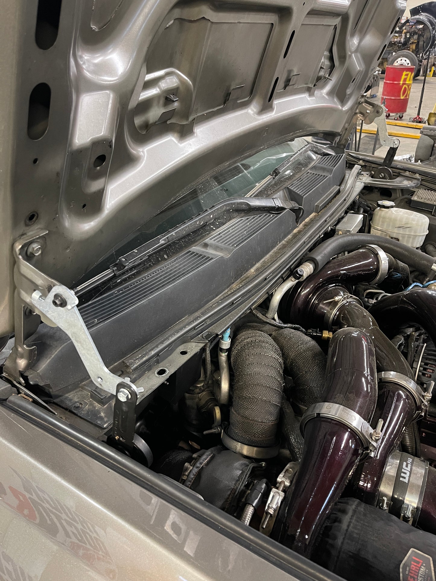 DP Customs High Access Hood Brackets installed on a 2007.5-2016 GM truck showing the sturdy metal brackets and mounting hardware
